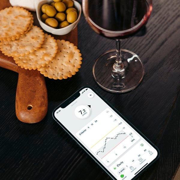 Un téléphone posé sur une table à côté d'une collation de fête montre l'application Dexcom G7 et ses informations sur le glucose.